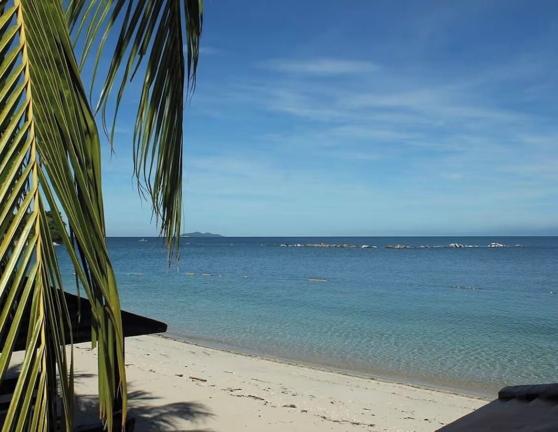 A beach with clear water and a distant view of a rocky coastline.