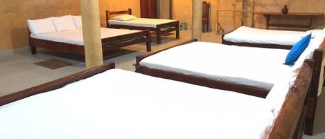 A room with three wooden beds, each with white bedding. There is a wooden table and a chair in the room.