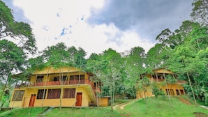 A two-story yellow building with a balcony, surrounded by lush greenery and a clear sky. - Sinharaja Eco Lodge  (Neluwa)
