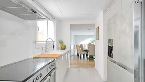 A modern kitchen with a stainless steel stove, a sink, and a refrigerator. There is a dining area with a table and chairs visible in the background.