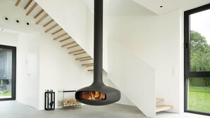 Un intérieur moderne avec une cheminée centrale, un escalier et de grandes fenêtres.