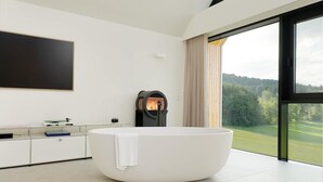 Une salle de bain moderne avec une baignoire sur pieds, une grande fenêtre donnant sur un paysage verdoyant et un téléviseur à écran plat fixé au mur.
