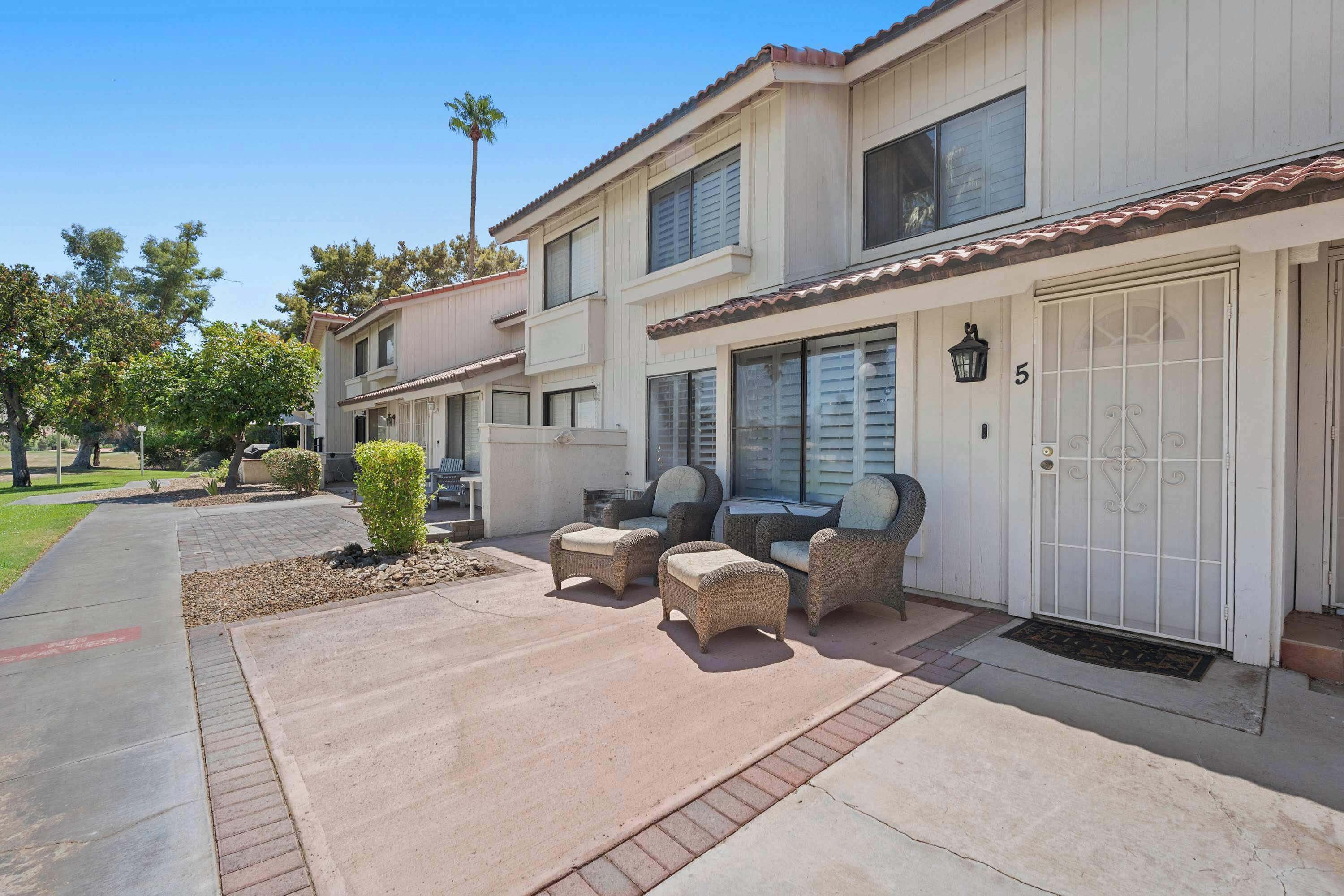 A two-story residential building with a covered patio area featuring outdoor furniture.