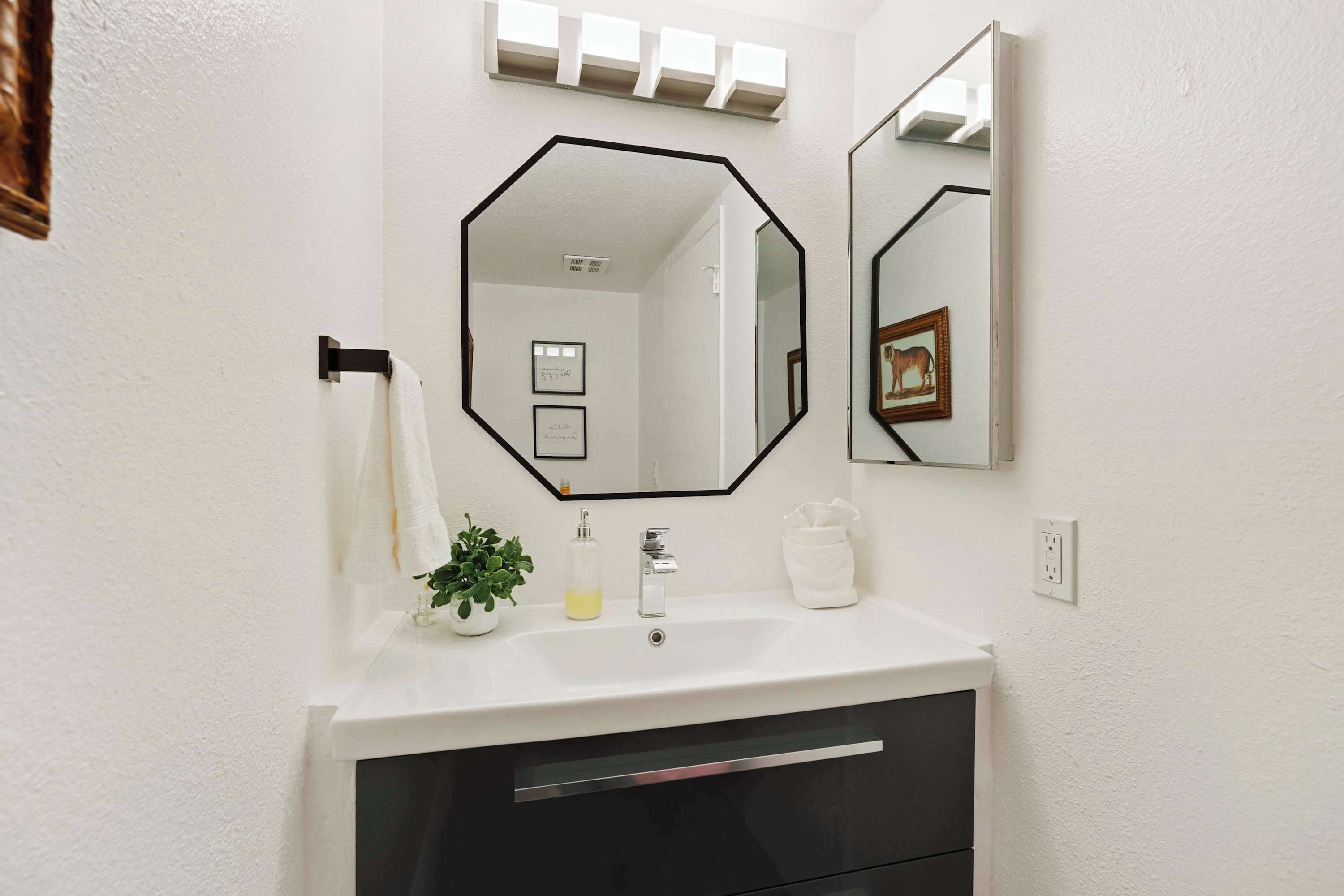A bathroom with a white sink, black vanity, and a large octagonal mirror.