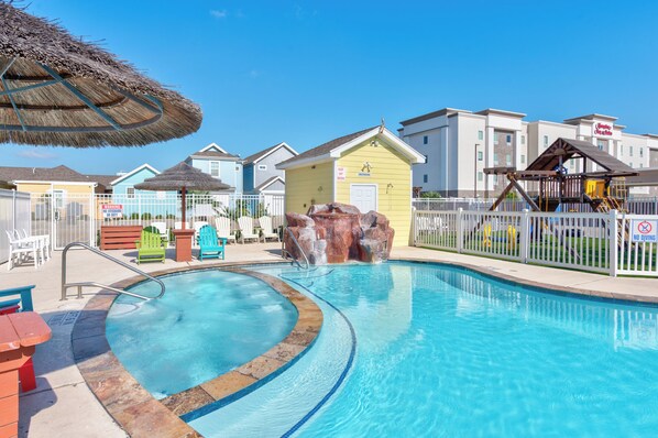 A swimming pool with a thatched umbrella, a play structure, and a building with a 'No Diving' sign.