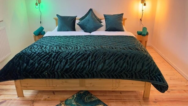 Ein Bett mit einer dunkelgrünen Steude, einem Holzkopfteil und zwei Nachttischen mit grünen Kissen.