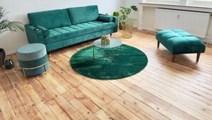 Ein Wohnzimmer mit einem petrolfarbenen Sofa, einem runden Couchtisch und passendem Hocker.