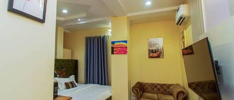A compact hotel room with a bed, a sofa, a small table, and a TV.