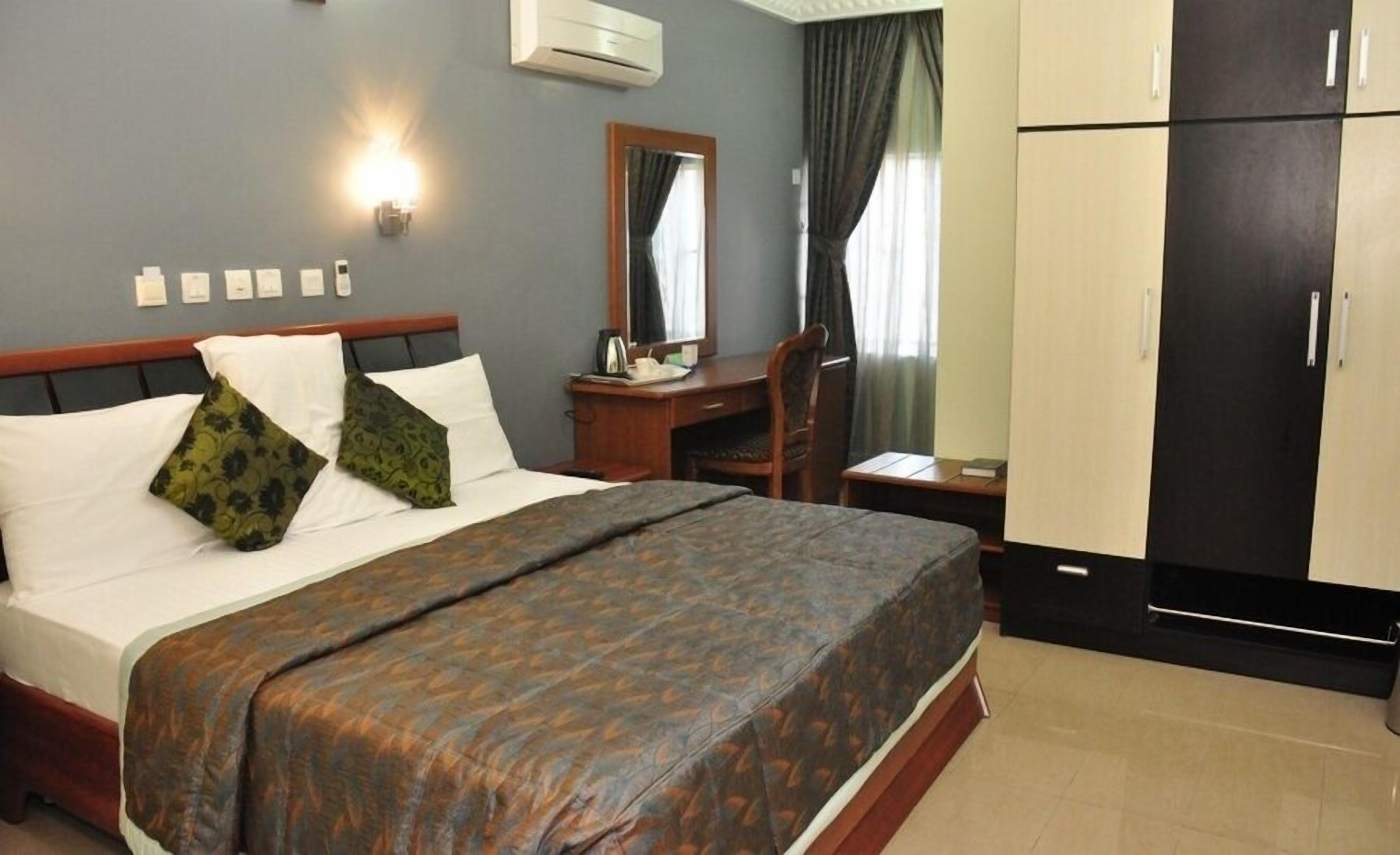 Una habitación de hotel con cama, escritorio, silla, armario y unidad de aire acondicionado.