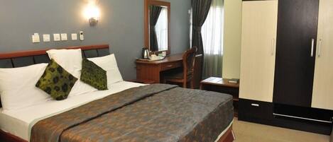 Una habitación de hotel con cama, escritorio, silla, armario y unidad de aire acondicionado.