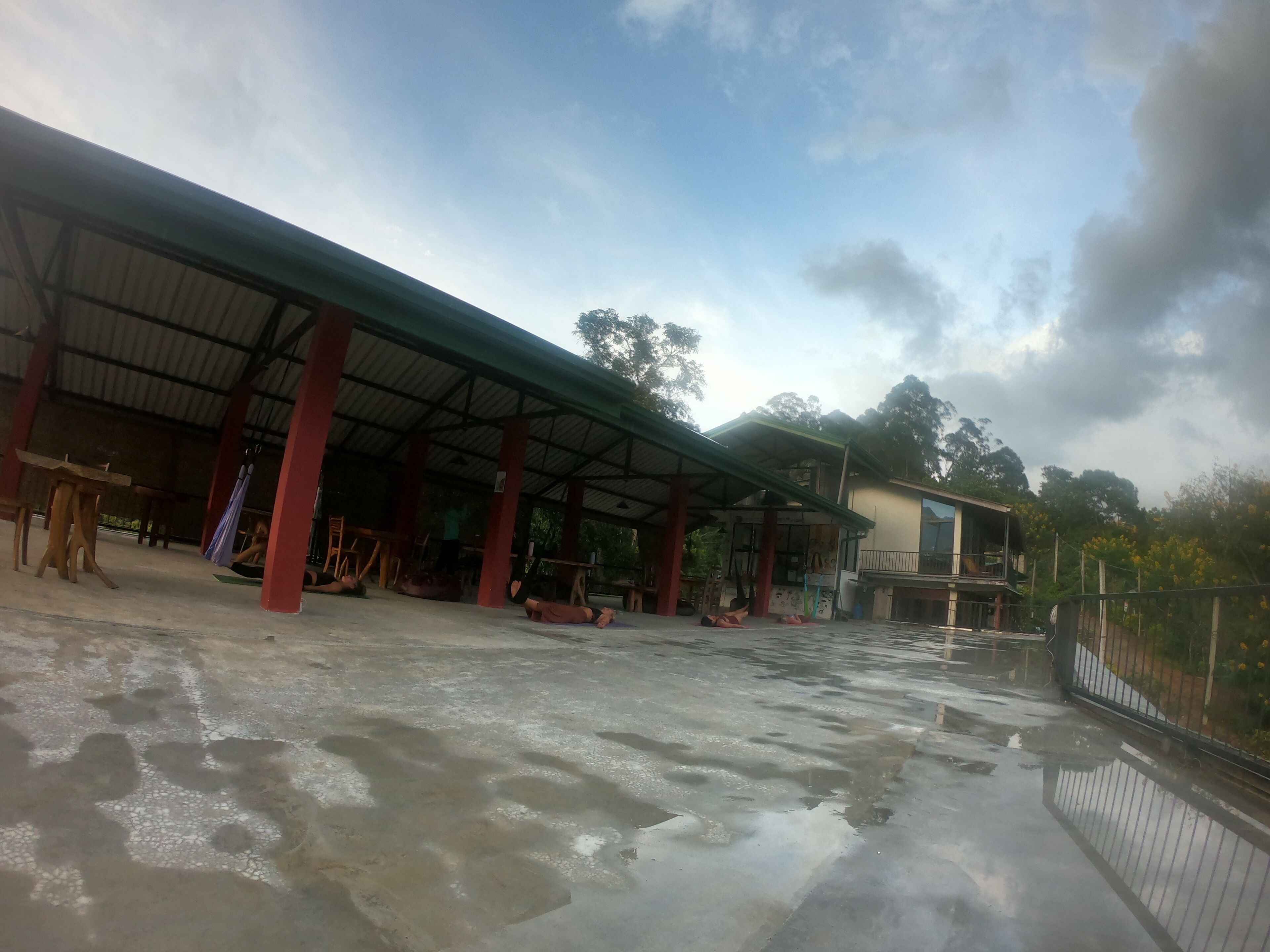 A covered outdoor area with a concrete floor, red pillars, and a building in the background.