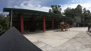 An outdoor covered area with a concrete floor, red pillars, and a table with chairs.