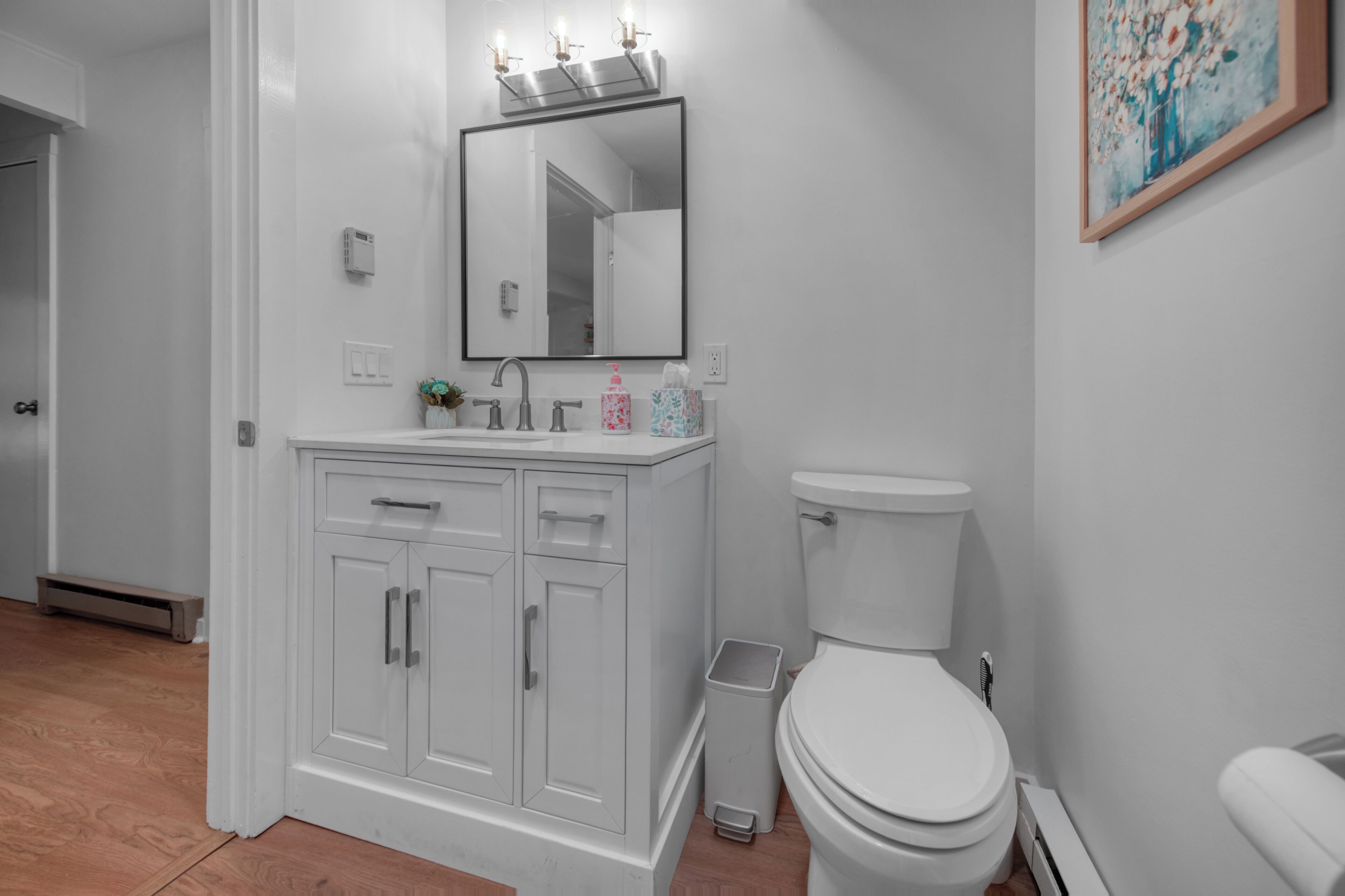 A bathroom with a white vanity, a mirror, a toilet, and a trash can.