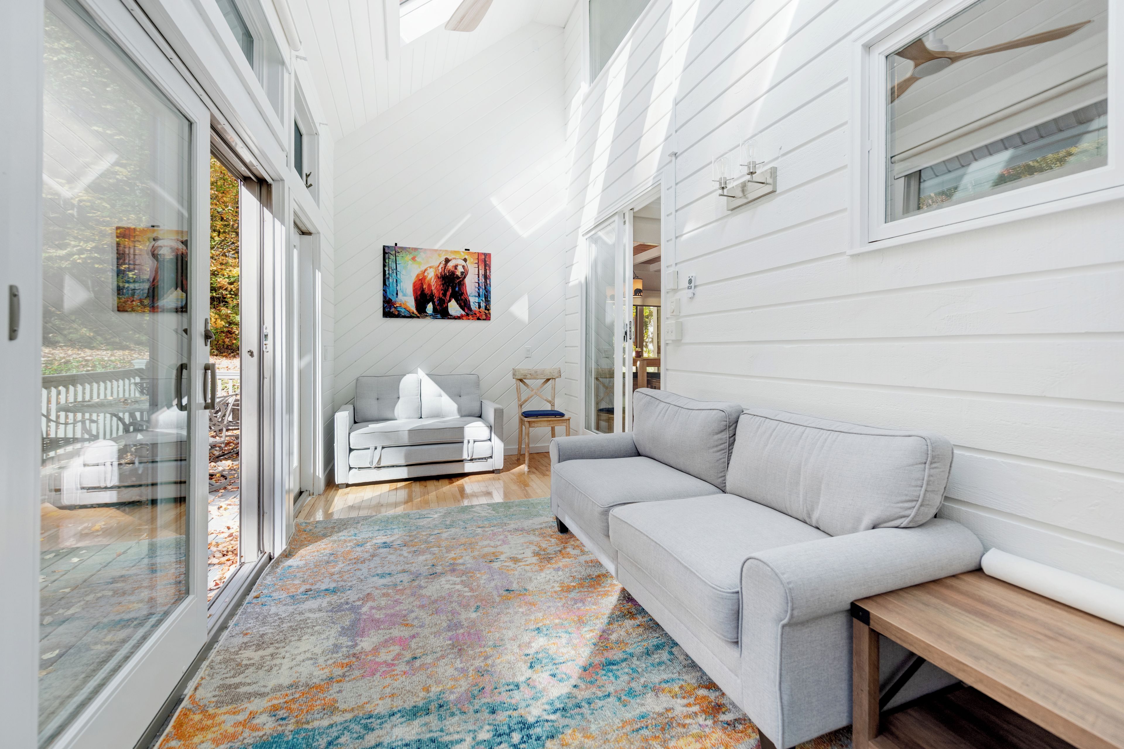 A modern interior with a grey sofa, a colorful rug, and a painting of a bear on the wall.