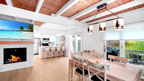 A modern kitchen with white cabinets and a large island, a dining area with wooden furniture, and a fireplace with a visible fire. - 3 bedroom Chic condo - Community pool and tennis - 1 Mile to Mount Snow (Dover)