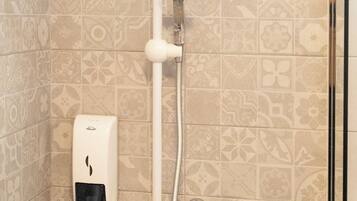 A shower with a handheld showerhead, a wall-mounted soap dispenser, and a handrail.
