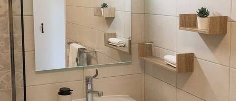 Un baño con un lavamanos blanco, un espejo y estanterías de madera con plantas.