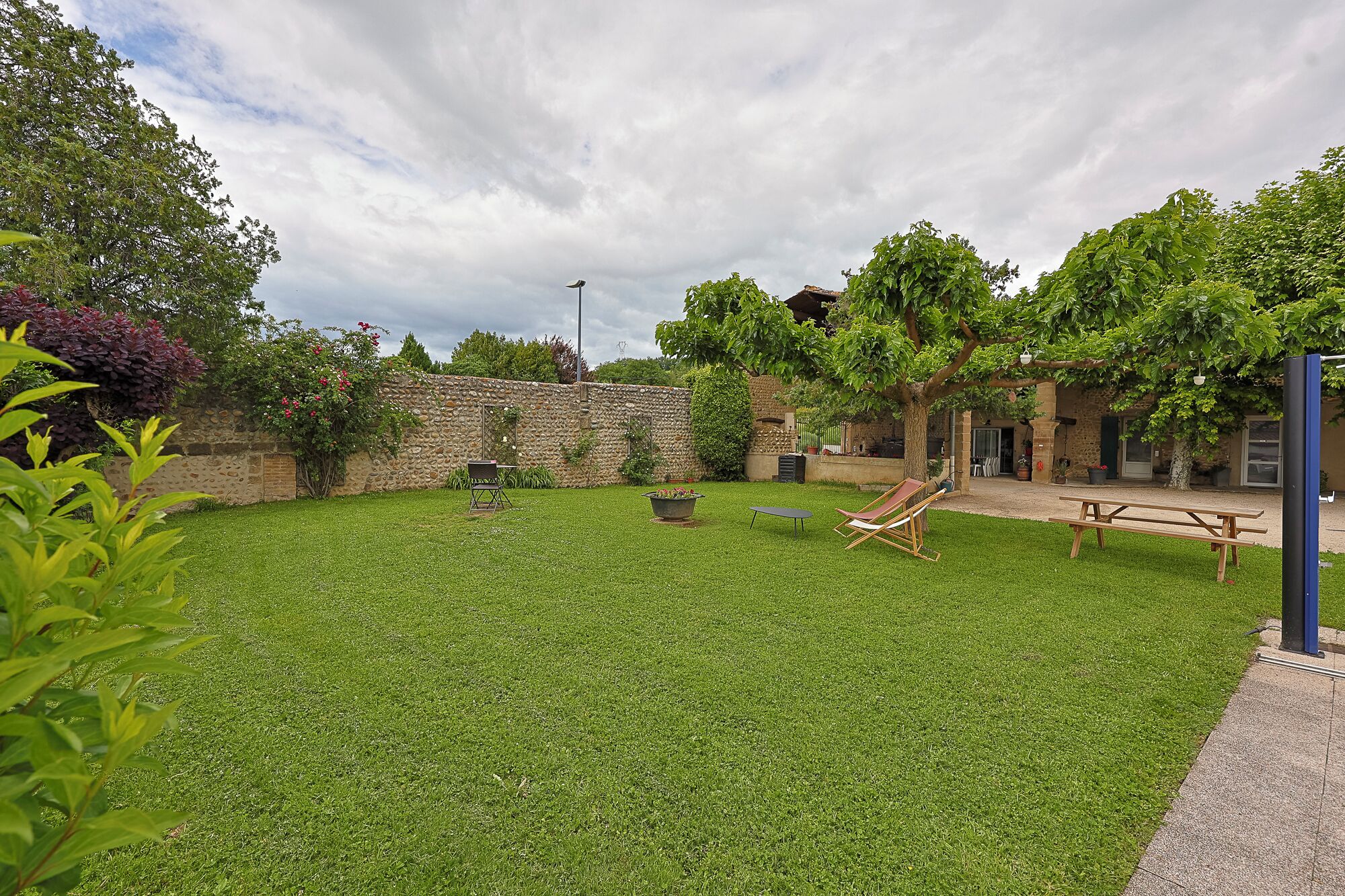 Un patio trasero bien cuidado con un muro de piedra, césped y mobiliario exterior, incluyendo una mesa y sillas.