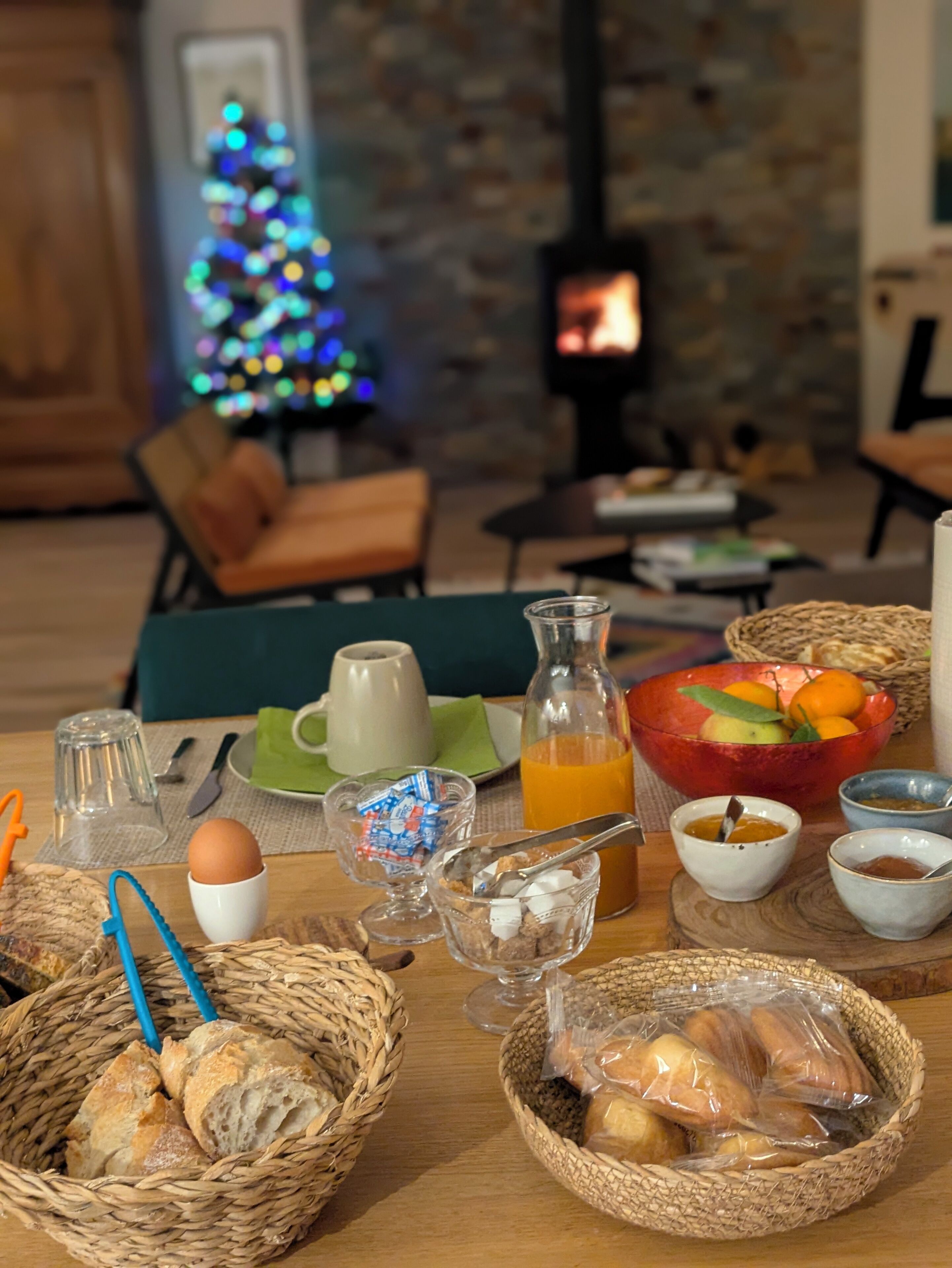 A breakfast table with bread, eggs, juice, and a Christmas tree in the background.