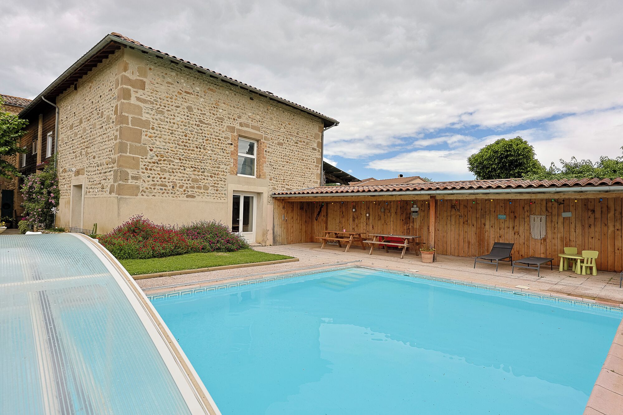 Un bâtiment en pierre doté d’une piscine, d’une terrasse en bois et d’un espace salon extérieur.