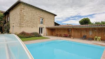 Un bâtiment en pierre doté d’une piscine, d’une terrasse en bois et d’un espace salon extérieur.