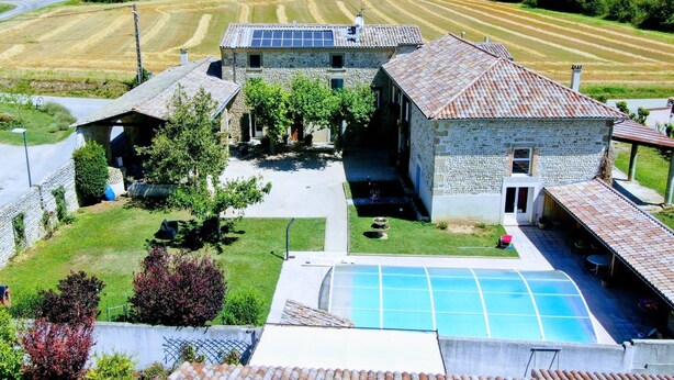 Un edificio in pietra con piscina, immerso in un paesaggio verdeggiante e campi.
