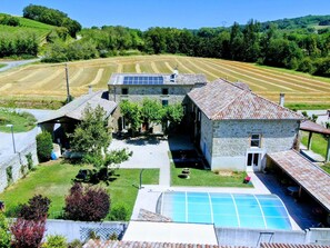 Un bâtiment en pierre doté d’une piscine, entouré d’un paysage verdoyant et luxuriant ainsi que de champs.