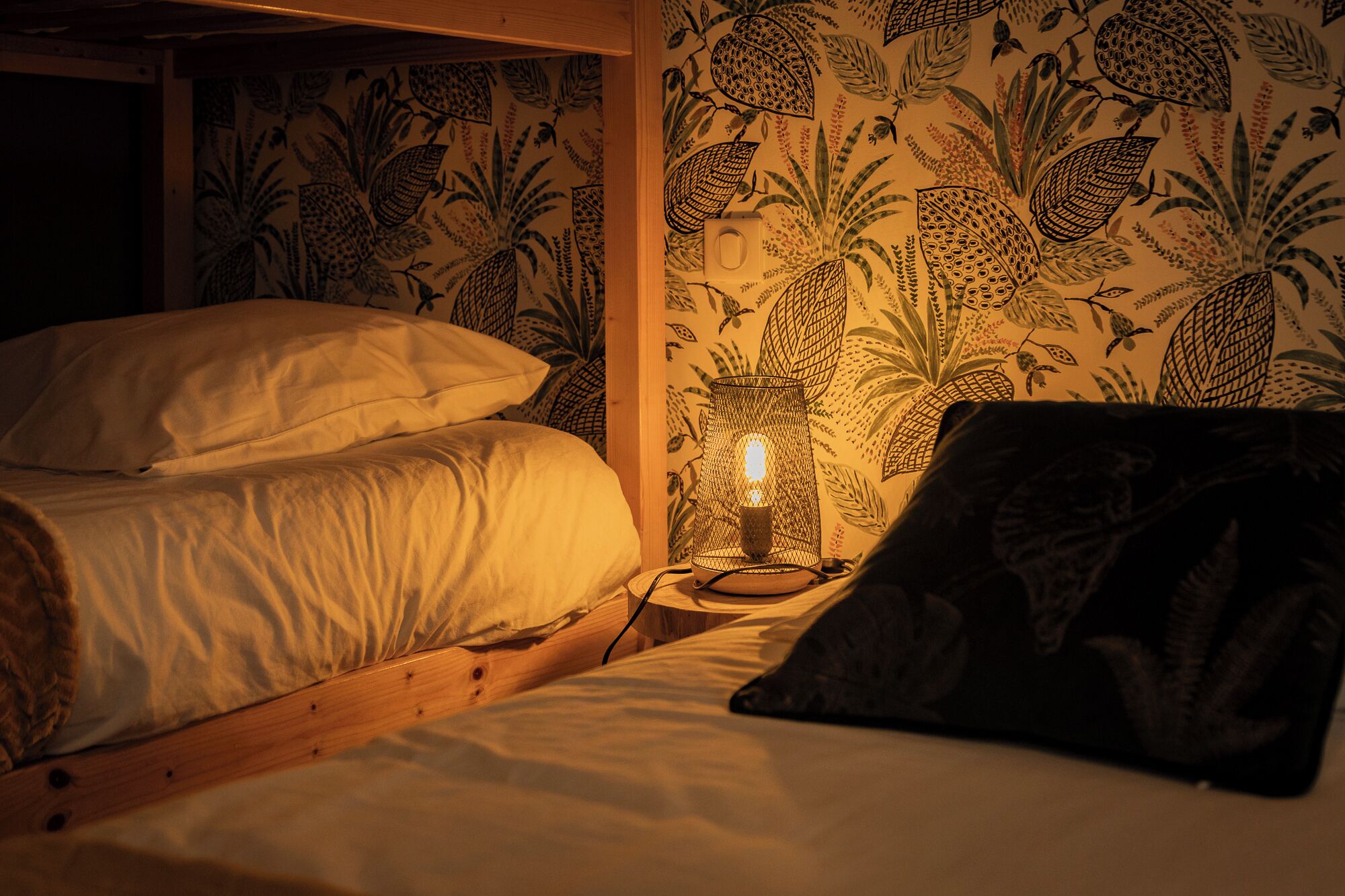 Una habitación con dos camas, una mesita de noche con lámpara y un papel tapiz estampado.