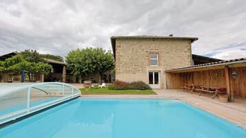 Relax by the serene pool surrounded by lush greenery and a rustic building.