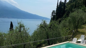 Piscina retangular com água azul cristalina, rodeada por um deck ladrilhado e cadeiras de sol brancas.