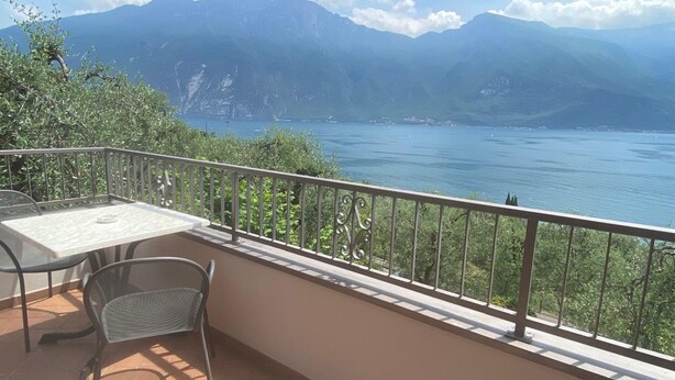 Uma varanda com mesa e cadeiras, vista para um lago e montanhas.