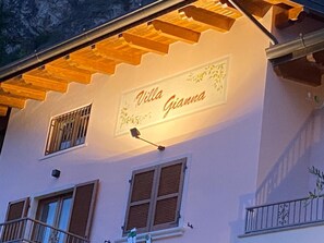 Villa Gianna met een bord bij de gevel, houten luiken aan de ramen en een balkonhek.