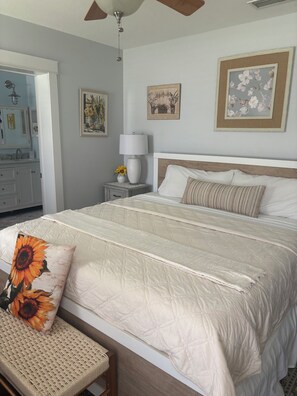 Quarto com cama, mesa de cabeceira, abajur e quadros na parede.