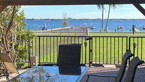 An outdoor patio with a glass table and chairs, overlooking a waterfront with a dock and palm trees. - Lake Jackson beachfront home w/dock, pool table, close to restaurants/shops (Sebring)