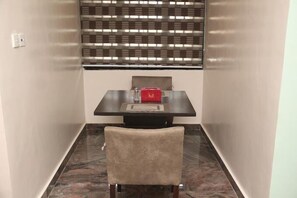 A small dining area with a table and chair, a window with blinds, and a red box on the table. - The Coral Luxury Apartment (Abuja)