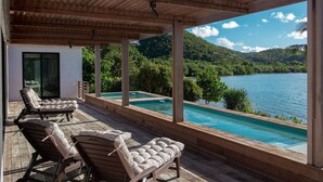 A wooden deck with lounge chairs overlooking a swimming pool and a lake. - Monarch Cottage Waterfront Fish Bay, Pebble shoreline, A/C, Generator (St. John)