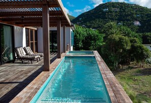 A rectangular pool with a wooden deck and lounge chairs, surrounded by greenery and a mountain backdrop. - Monarch Cottage Waterfront Fish Bay, Pebble shoreline, A/C, Generator (St. John)
