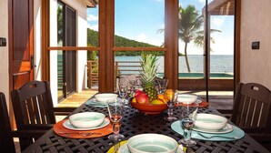 A dining table set for two with a view of the ocean and palm trees. - Monarch Cottage Waterfront Fish Bay, Pebble shoreline, A/C, Generator (St. John)
