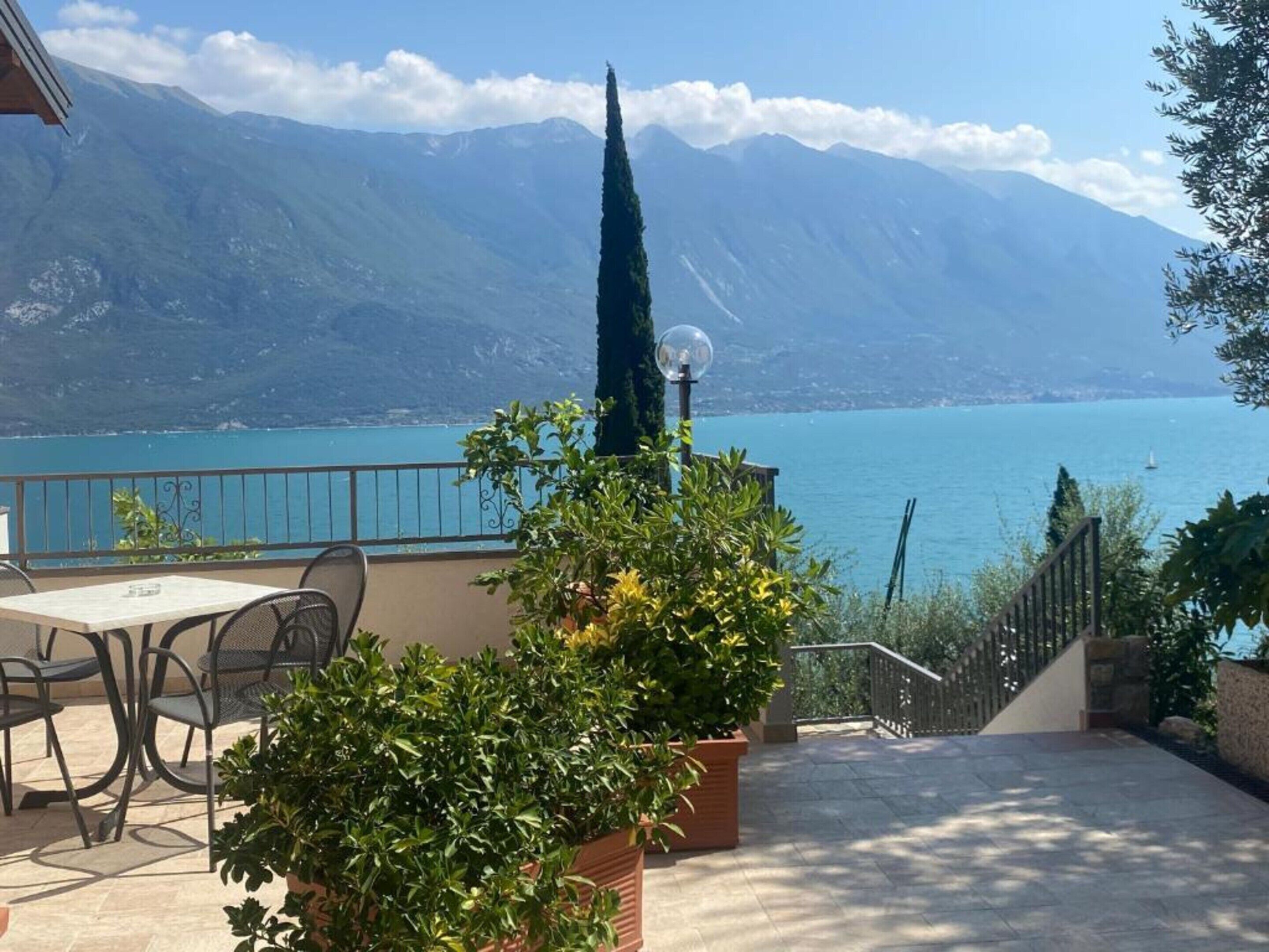 A terrace with a table and chairs, overlooking a lake with mountains in the background.