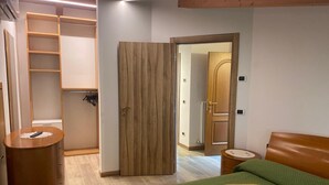 A bedroom with a bed, a wooden wardrobe, a bedside table, and a door leading to another room.