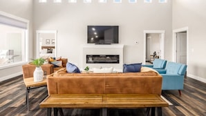 Ein geräumiges Wohnzimmer mit einem großen, braunen Ecksofa, einem blauen Sessel, einem Holztisch und einem Flachbildfernseher, der über einem Kamin angebracht ist.