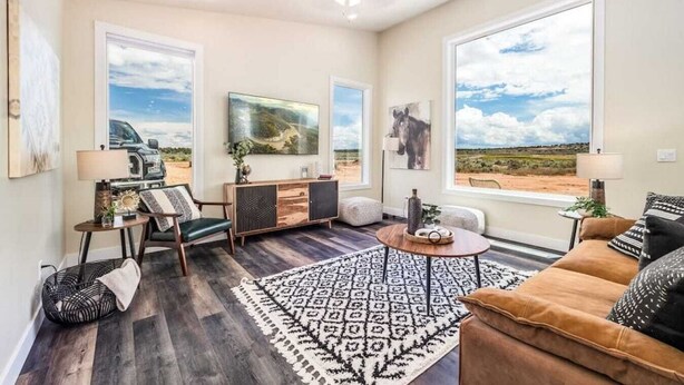 A spacious living room with large windows, a wooden floor, a brown sofa, a coffee table, and a rug.