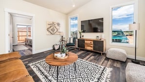 A living room with a large TV, a wooden coffee table, a patterned rug, and a view of a car through a window.