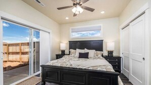 A bedroom with a large bed, a ceiling fan, and a sliding glass door leading to a patio.