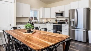 A modern kitchen with white cabinets, stainless steel appliances, and a wooden dining table with chairs.