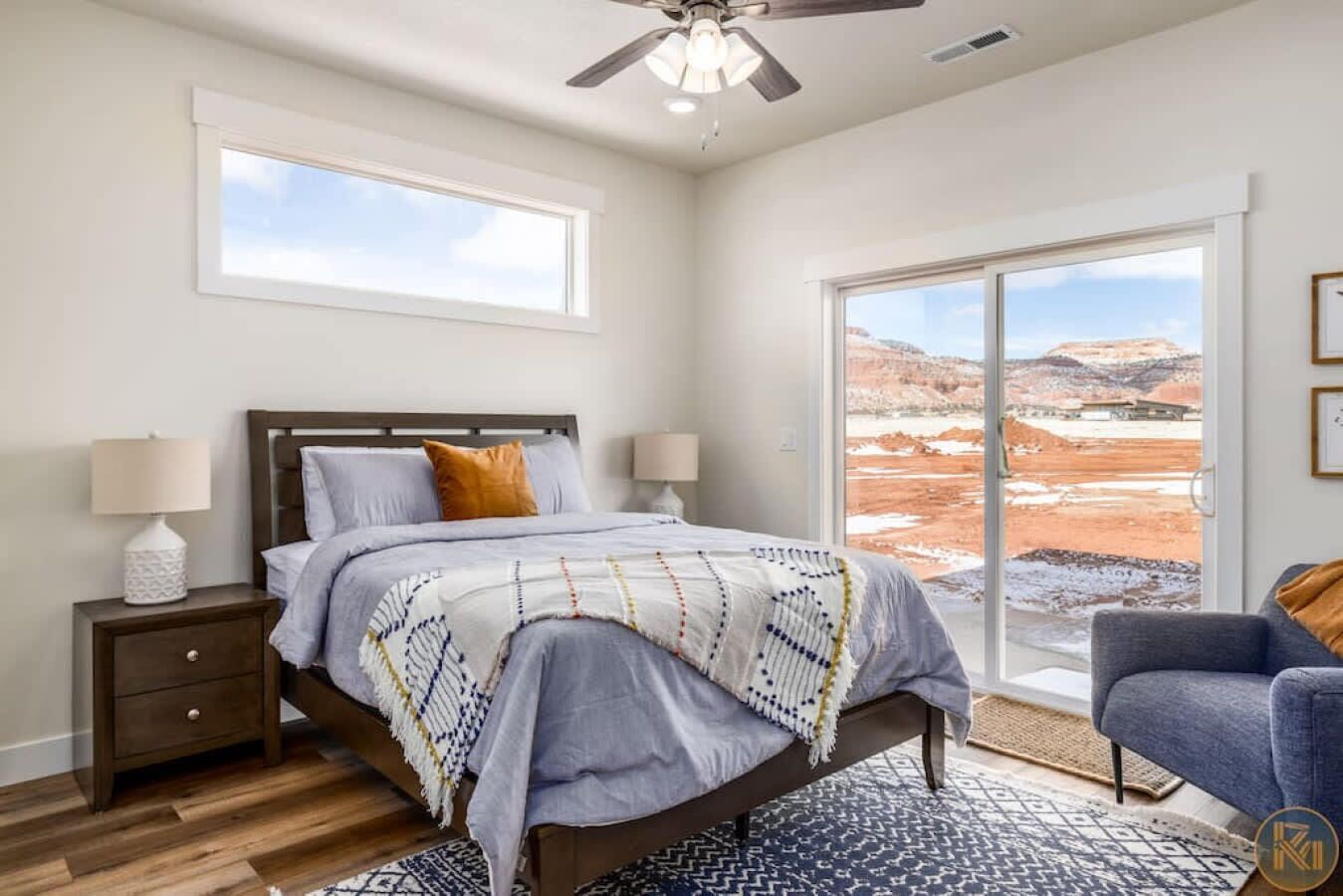 Une chambre à coucher comprenant un lit, deux lampes de chevet, une table de chevet, une chaise, une grande fenêtre avec vue et un ventilateur de plafond.