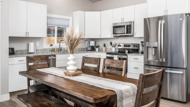 Une cuisine moderne avec des meubles blancs, des appareils en acier inoxydable et une table à manger en bois.
