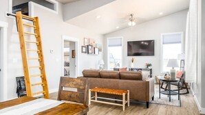 Un salon spacieux avec une table en bois, un canapé marron et une échelle appuyée contre le mur.