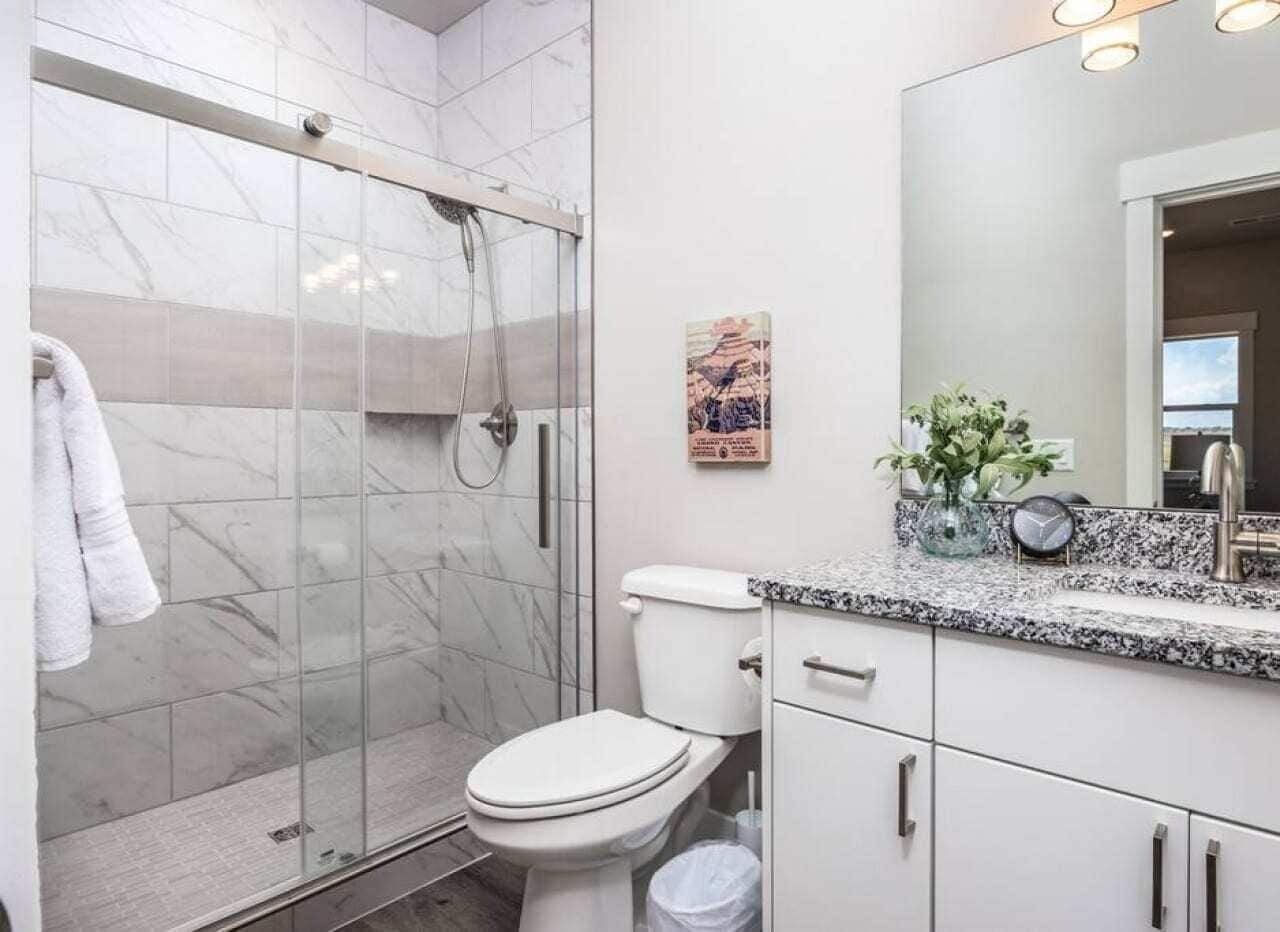 A modern bathroom with a glass-enclosed shower, a toilet, and a vanity with a sink and mirror.