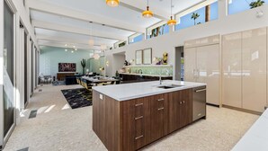 A modern kitchen with a large island, pendant lighting, and a view of the outdoors. - Webb House – Mid-Century Modern in Vista Las Palma (Palm Springs)